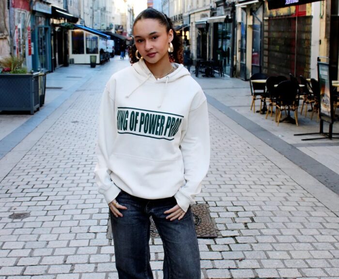 Une jeune femme portant un pull blanc avec la marque "kingofprod" imprimer dessus.